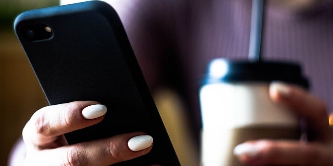 Person håller en smartphone bredvid en kopp kaffe