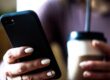 Person håller en smartphone bredvid en kopp kaffe