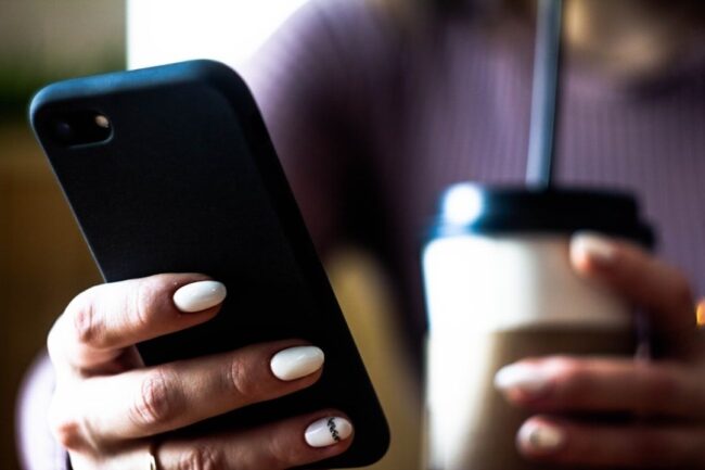 selected-01-person-scrolling-smartphone-morning-coff-optimized Person håller en smartphone bredvid en kopp kaffe