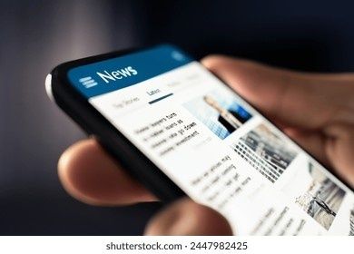 Hand håller en smartphone med ett digitalt nyhetsflöde på skärmen